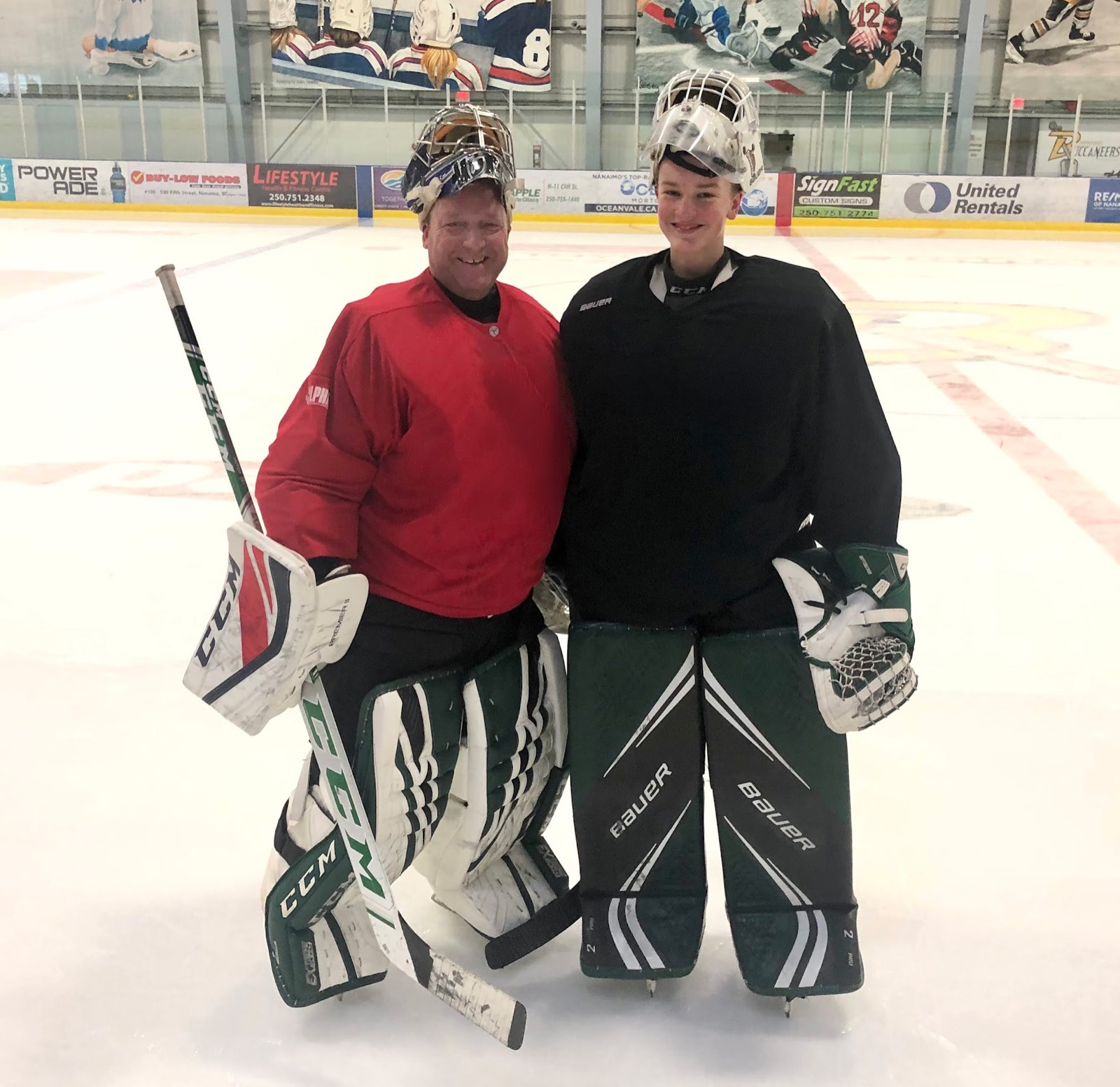 A goalie dad and a young goalie, both in full gear, on the ice together