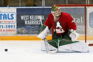 West Kelowna Warriors goalie Devan Dubnyk in red jersey making a blocker save during practice, puck visible in front of cr...