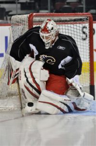 Miikka Kiprusoff in butterfly stance making a glove save during Calgary Flames practice in black jersey and red-white pads