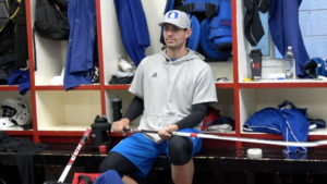 Carey Price sits in the Montreal Canadiens locker room in casual attire, holding a goalie stick between periods.