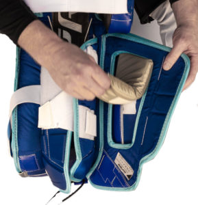 Hands adjusting a removable calf pillow insert inside a blue and teal goalie leg pad interior