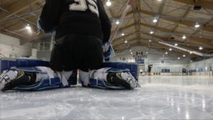 Hockey goalie in butterfly position showing Bauer UltraSonic pads knee stack detail from ice-level view