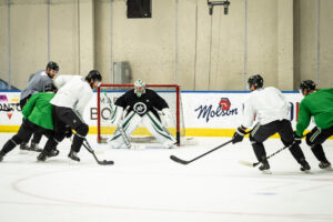 Anton Khudobin in butterfly stance facing shooters during NHL practice drill at indoor rink