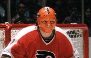 Philadelphia Flyers goalie Doug Favell in vintage orange fiberglass mask and red Flyers jersey crouched in crease