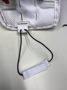 Close-up of white Bauer goalie pad toe elastic strap attachment loop detail showing hardware connection point