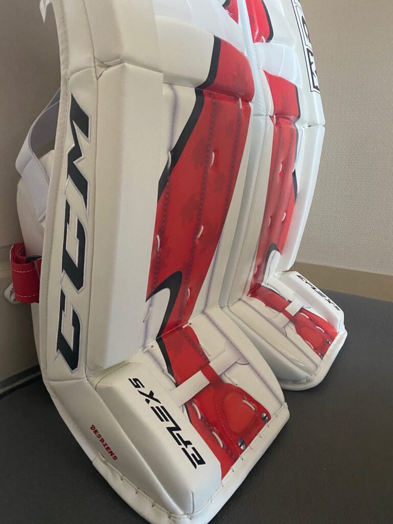 CCM goalie leg pads in white and red, Team Canada colorway, displayed upright showing knee rolls and boot straps