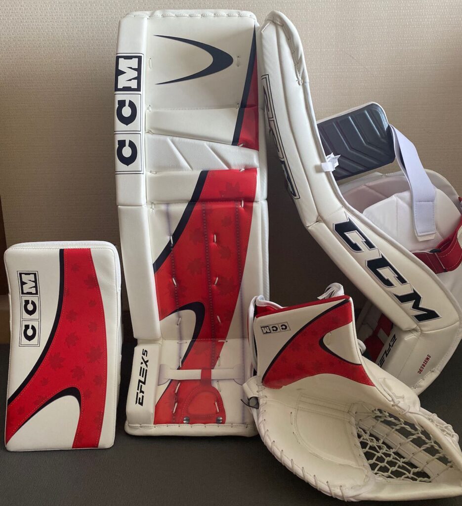 CCM goalie gear set in white and red Team Canada colorway, including leg pads, blocker, and trapper displayed on a surface