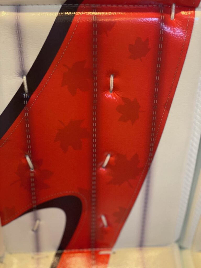Close-up of Team Canada red goalie pad featuring maple leaf graphic detail and stitching