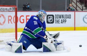 Thatcher Demko making a blocker save in Vancouver Canucks blue and green pads, tracking a loose puck in crease