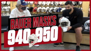 Two people examining Bauer 940 and 950 goalie masks in a locker room during equipment review