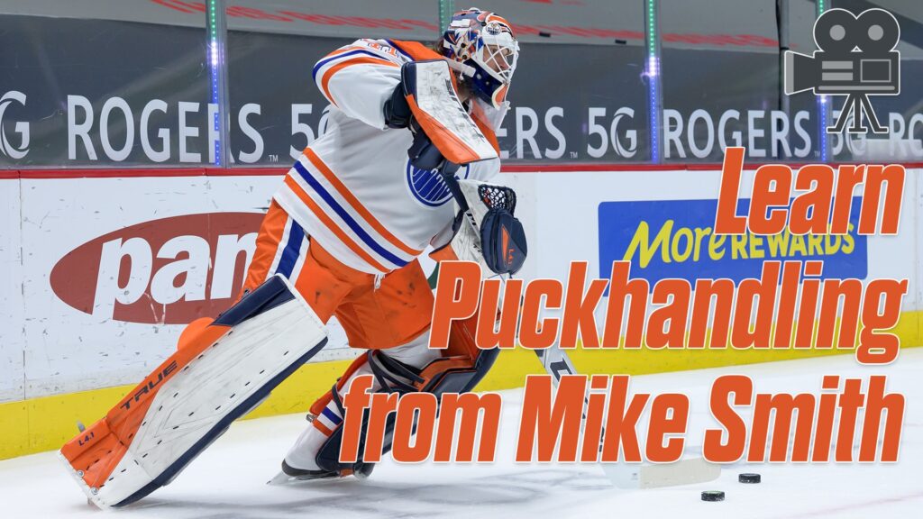 Edmonton Oilers goalie Mike Smith handles the puck behind the net in full gear, wearing white, orange, and blue equipment.