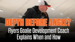 Brady Robinson, Philadelphia Flyers goalie development coach, on ice in black jacket and Flyers cap during practice session.