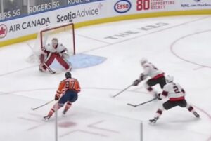 Joey Daccord in white Kraken gear squares up in butterfly as McDavid drives the net during an Oilers power play sequence.