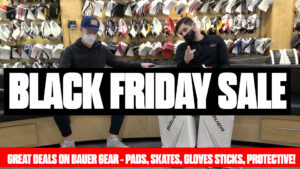 Two masked staff pose in front of Bauer goalie gear display for Black Friday sale on pads, skates, gloves, sticks and prot...