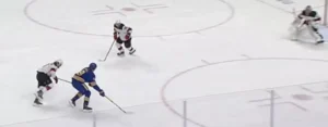 Eric Comrie in white Jets gear reads the play from his crease as Jack Eichel drives down the wing with a defender trailing.