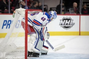 New York Rangers goalie #40 crouches behind the net in white pads and mask during an NHL game.