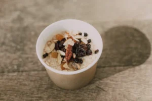 Cup of oatmeal topped with dried fruit, nuts, and chocolate chips — a high-protein pre-game snack for hockey goalies