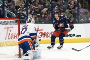 Ilya Sorokin holds his stick on his shoulder in butterfly stance as a Columbus Blue Jackets skater cuts toward the net.