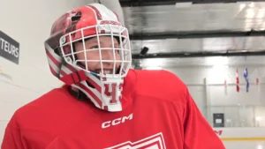 Goalie wearing CCM AXIS XF mask in red practice gear looks upward during on-ice training session