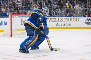 Jordan Binnington handles the puck behind the net in full St. Louis Blues blue gear during an NHL game.