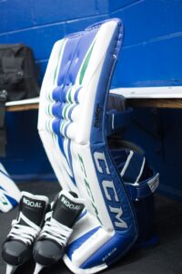 CCM Eflex 4 goalie leg pad in blue and white with green accents, displayed in locker room with skates nearby