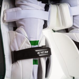 Close-up of CCM goalie pad knee strap system on white pads with green accents, showing secure binding hardware detail