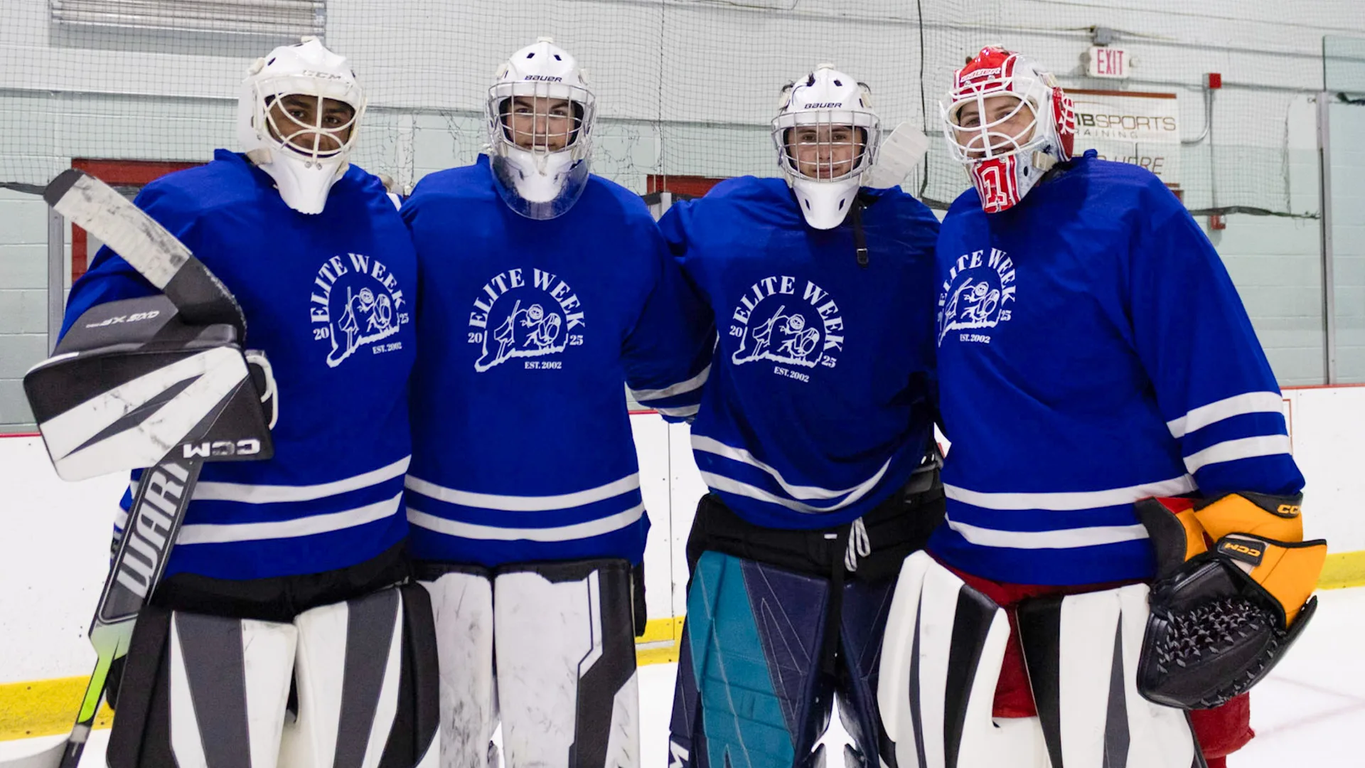Four Connecticut Crease students in blue jerseys posing together on the ice with pads and blockers at their facility...