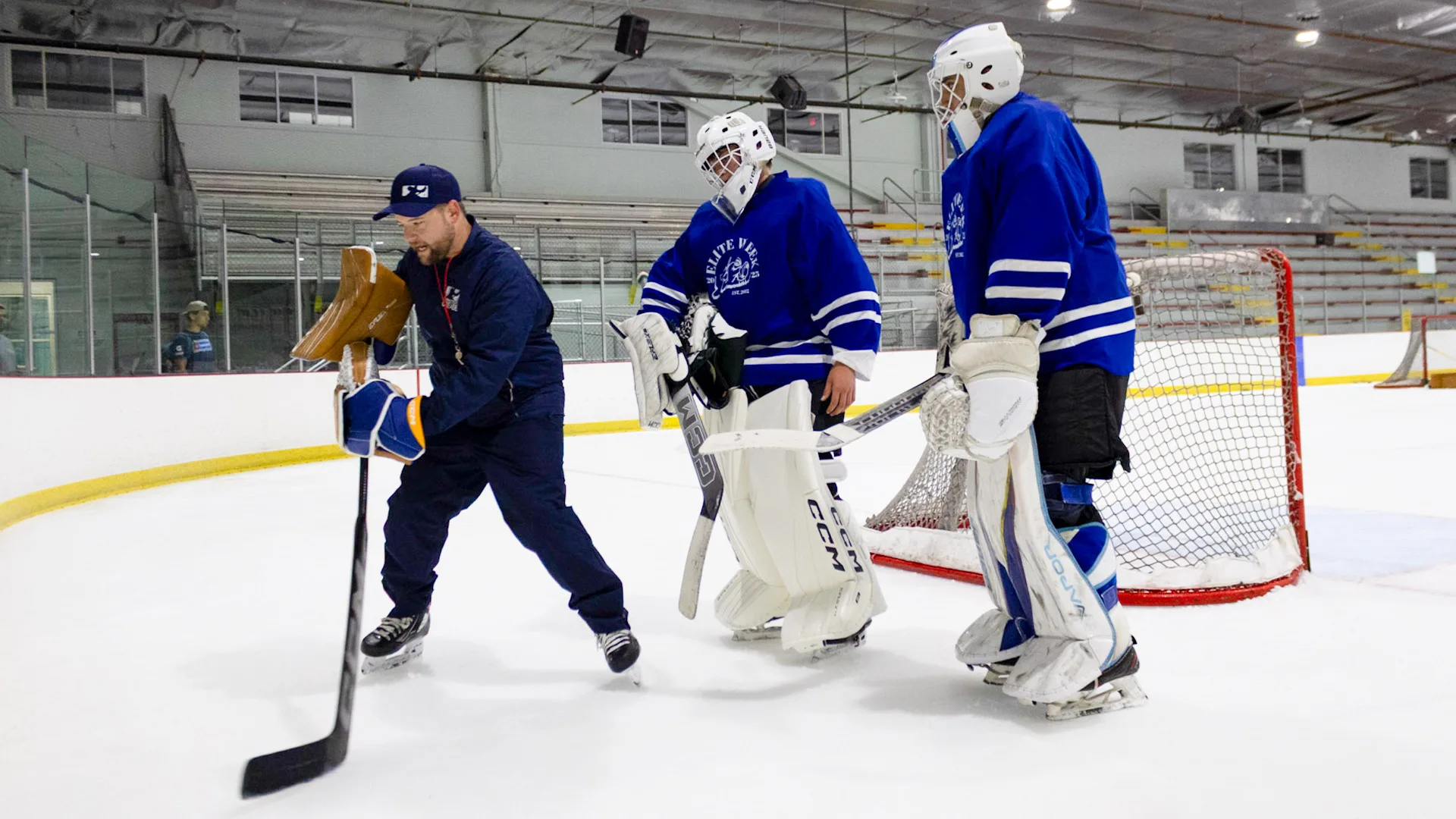Connecticut Crease goalie coach instructs two young goalies in full gear during on-ice training session in Northford, CT.
