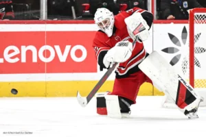 Carolina Hurricanes goalie Brandon Bussi in full gear handles the puck with his stick behind the net during a game.