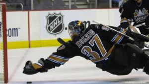 Olaf Kolzig #37 diving across crease in Washington Capitals black jersey making desperation save near post
