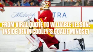 Calgary Flames goalie Devin Cooley in full butterfly stance making a save, wearing red and yellow Flames gear on home ice.