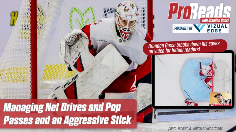 Brandon Bussi makes a paddle-down save in white Detroit Red Wings gear, aggressively challenging with his stick extended.