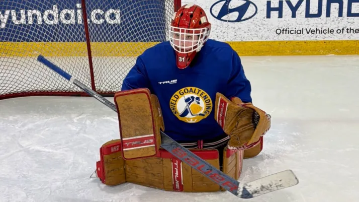 Shield Goaltending coach in butterfly position during on-ice session, wearing blue jersey, red helmet, and brown pads at C...