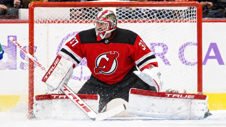 Photo illustration of Connor Hellebuyck in a New Jersey Devils jersey and white TRUE pads, set in his butterfly in front of the net